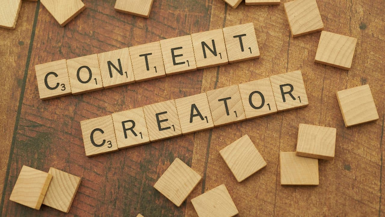 Wooden Scrabble tiles on a wood surface spelling the words Content Creator, with loose tiles scattered around them